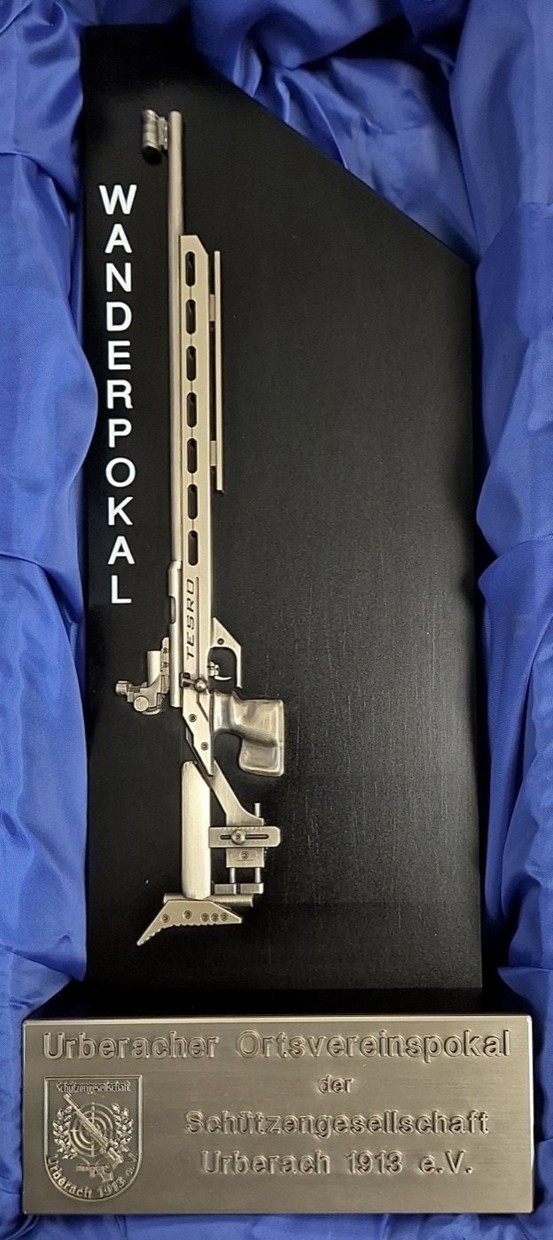 Der Wanderpokal des Urberacher Ortsvereinspokals: ein Kleinkalibergewehr
                      aus Metall auf schwarzer Tafel, darunter ein graviertes Schild mit dem
                      Vereinswappen